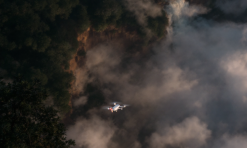 Drone capturing aerial footage over a dense forest at sunrise